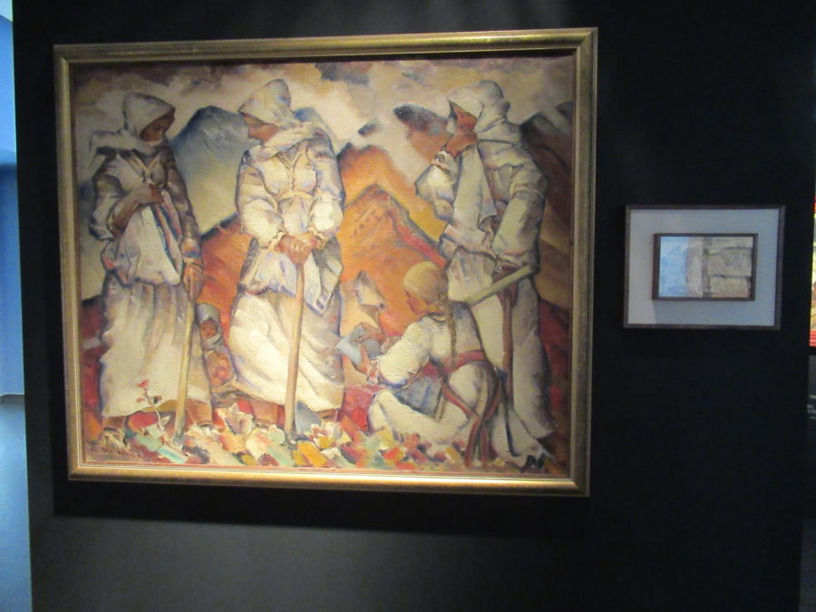 A painting depicting four women wearing all white and headscarves. Three are standing, one is crouched. Behind them are red mountains.